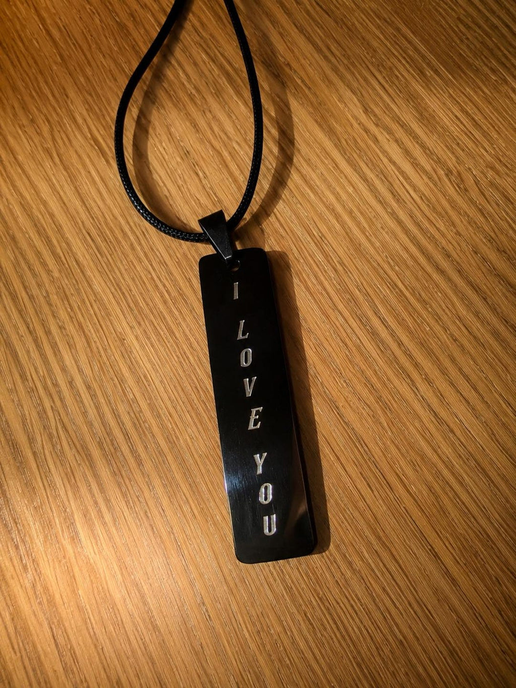 Black stainless steel bar pendant on a cord, engraved vertically